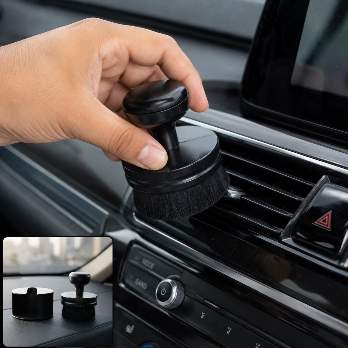 A hand holds a black detailing brush, cleaning a car's air vent, with a small inset showing the brush and its base on a