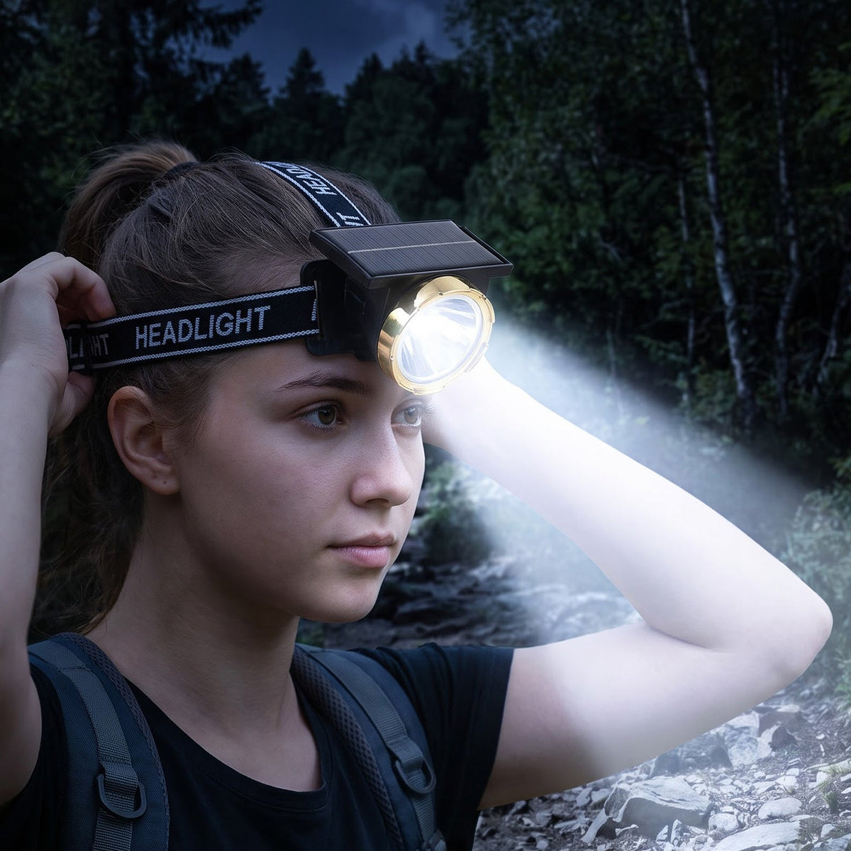 A young woman wearing a black and gold headlamp with a bright beam in a dark forest at night.