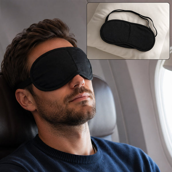 A man with a beard sleeps on an airplane wearing a black eye mask, with an inset of the mask on a pillow.