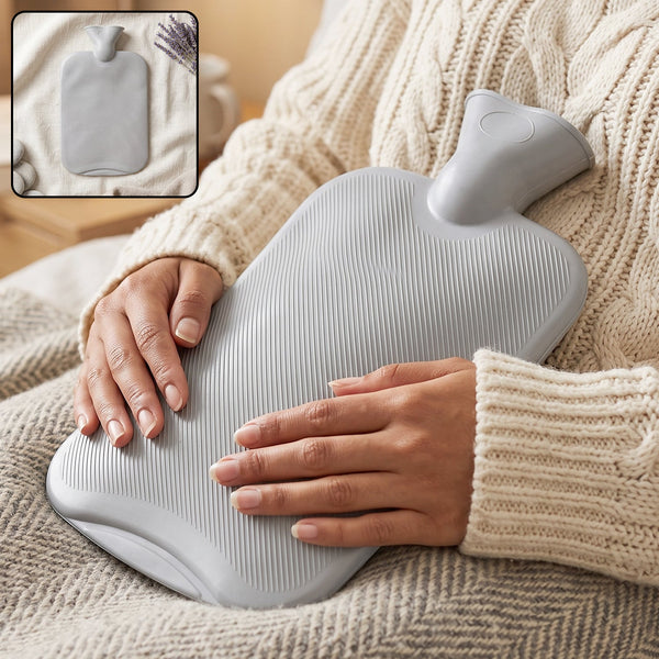 A person in a cream sweater holds a grey ribbed hot water bottle on their lap, with a small inset showing the bottle alone.