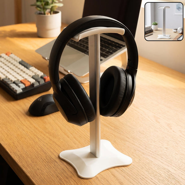 White and silver headphone stand holding black over-ear headphones on a wooden desk with a laptop.