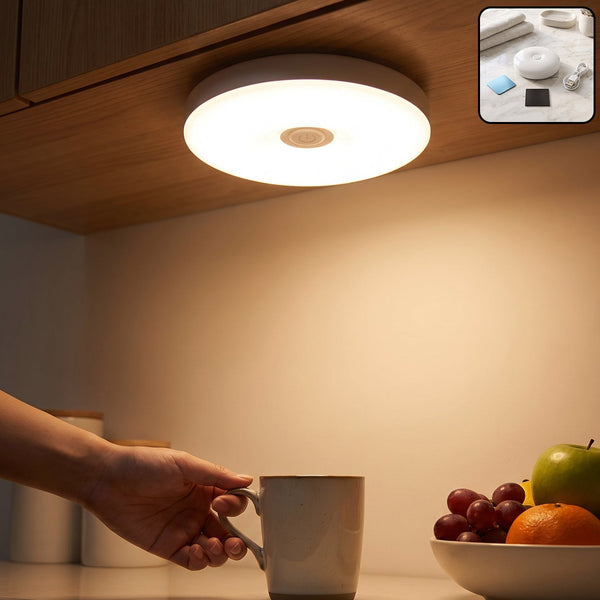 A hand reaches for a mug under a bright, round LED light mounted beneath a wooden cabinet, illuminating a fruit bowl.